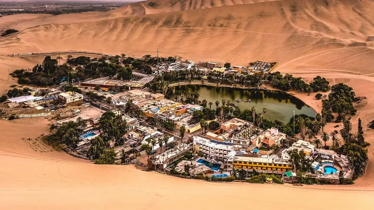 Oase Huacachina bei Ica, Peru, mit einem See, Hotels und Palmen, umgeben von riesigen Sanddünen.