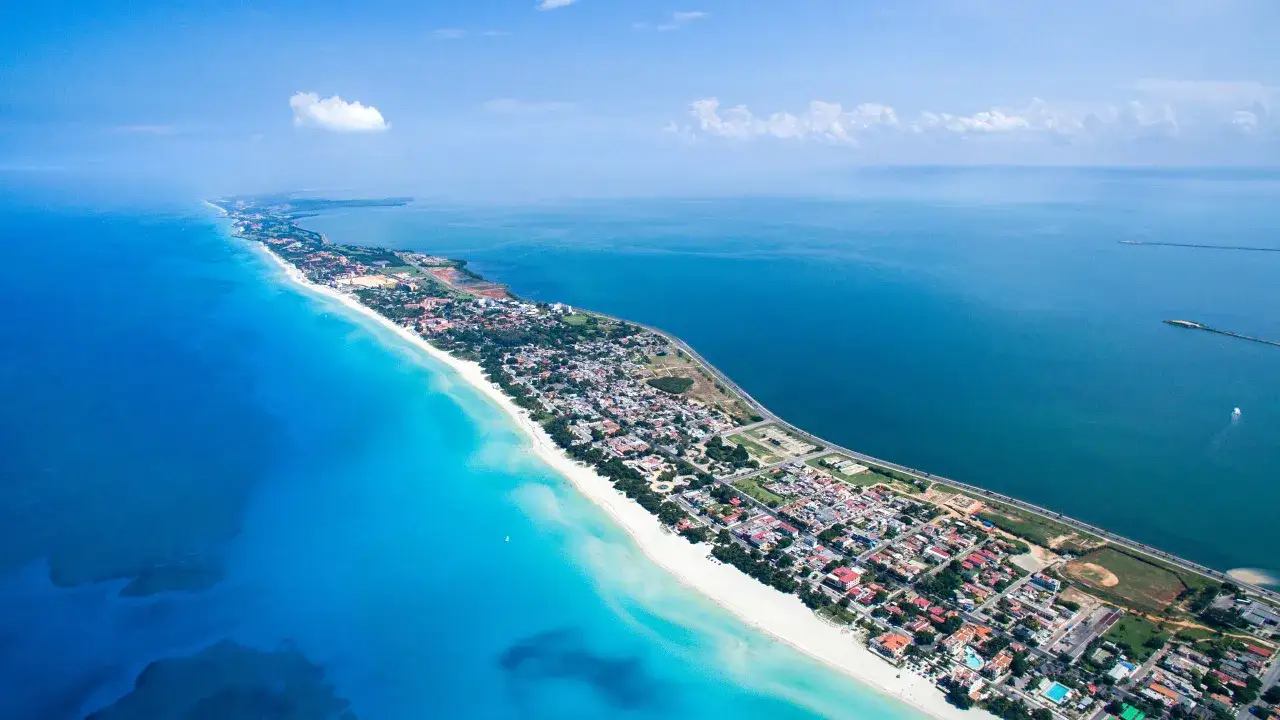 Luftaufnahme von Kuba Varadero: Ein langer, weißer Sandstrand trifft auf türkisfarbenes Wasser, gesäumt von einer Stadt mit roten Dächern.