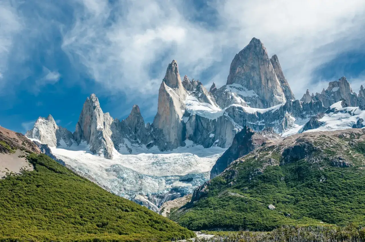 Majest&auml;tisches patagonia gebirge mit schneebedeckten Gipfeln, einem Gletscher und gr&uuml;nen H&auml;ngen unter einem dramatischen Himmel.