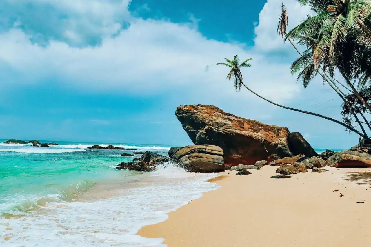 Traumhafter Strand mit Palmen und Felsen. Perfekt für die beste Reisezeit Sri Lanka Rundreise. Türkises Wasser und weißer Sand laden zum Entspannen ein.