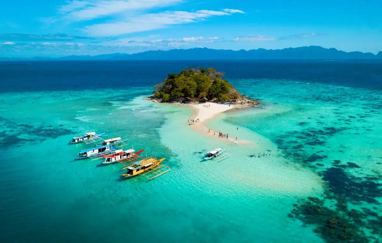 Traumhafte Philippinen Reisezeit: Boote ankern vor einer kleinen Insel mit Sandbank und türkisfarbenem Wasser.
