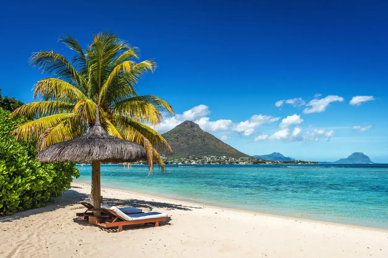 Traumhafter Strand auf Mauritius mit Palmen und Liegen. Keine Mauritius Reisewarnung, nur pure Entspannung am türkisfarbenen Meer.