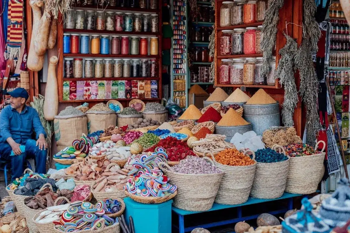 Bunter marokko markt mit Gewürzen, Kräutern und bunten Körben. Ein Mann sitzt im Hintergrund.