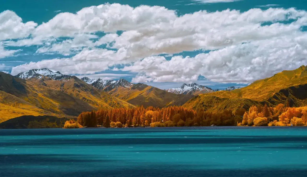 Herbstliche Farben in Neuseeland im November: goldene Berge, orange Wälder und ein türkisfarbener See unter dramatischen Wolken.