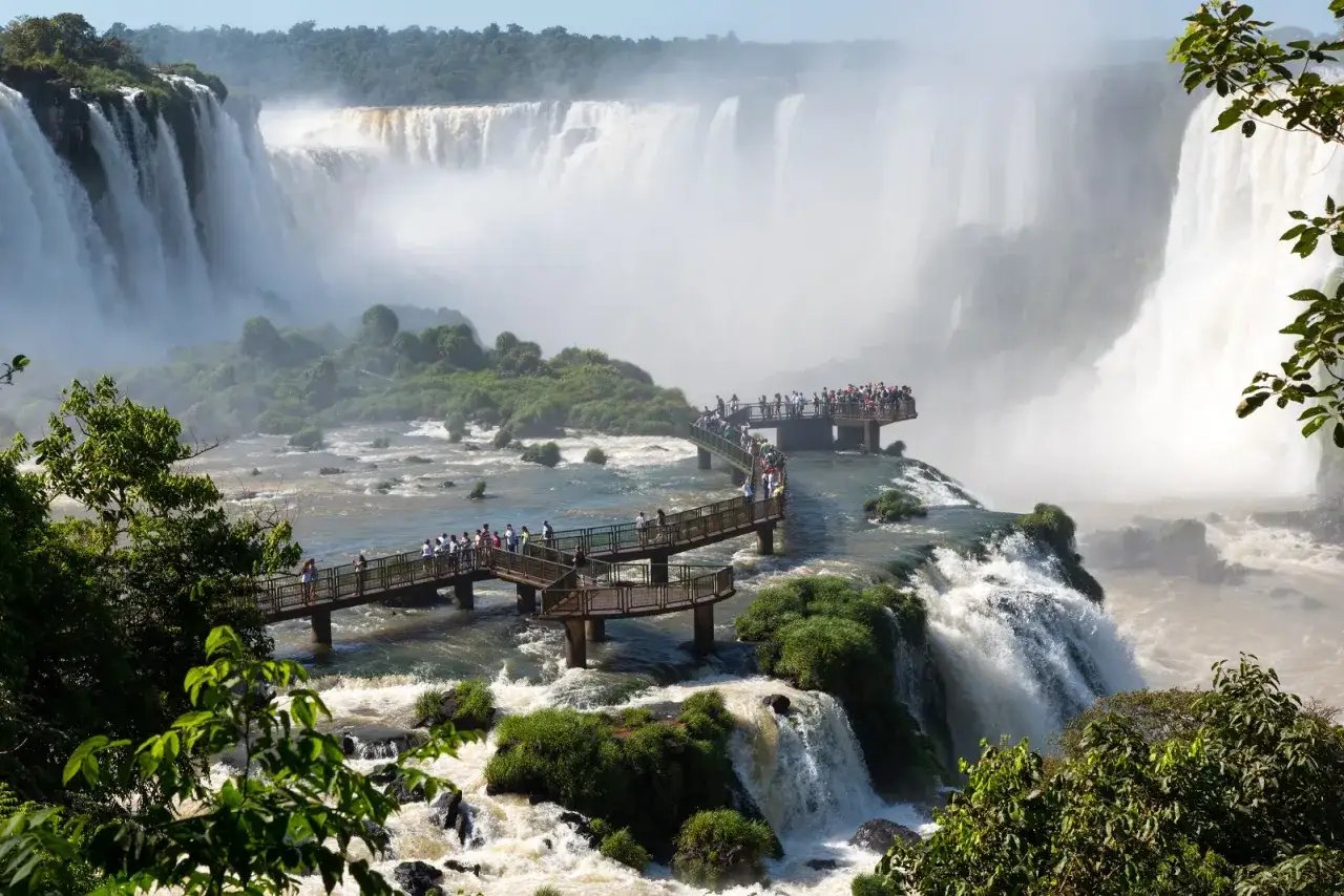 Besucher genießen die atemberaubende Aussicht auf die Foz de Iguaçu Wasserfälle von erhöhten Stegen aus, umgeben von üppigem Grün und tosendem Wasser.