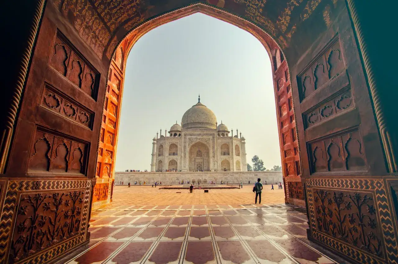 Durch ein kunstvoll verziertes Tor blickt man auf das Taj Mahal. Was ist das Taj Mahal? Ein Mausoleum, ein Meisterwerk der Architektur.