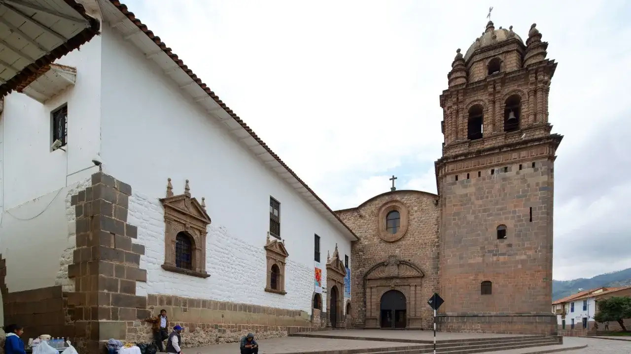 Historische Gebäude mit Glockenturm in Cusco, Peru. Menschen sitzen auf den Stufen vor einer Kirche.