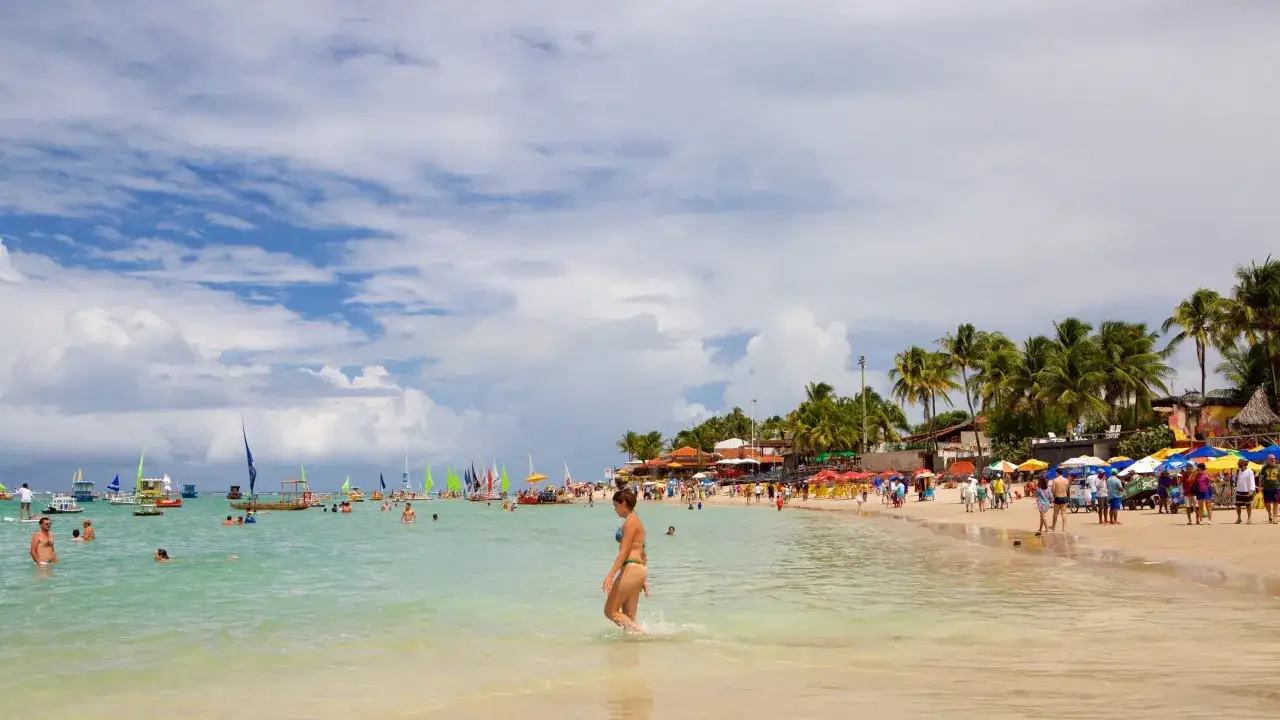 Sonniger Strand von Porto de Galinhas mit vielen Segelbooten, Palmen und Badegästen.