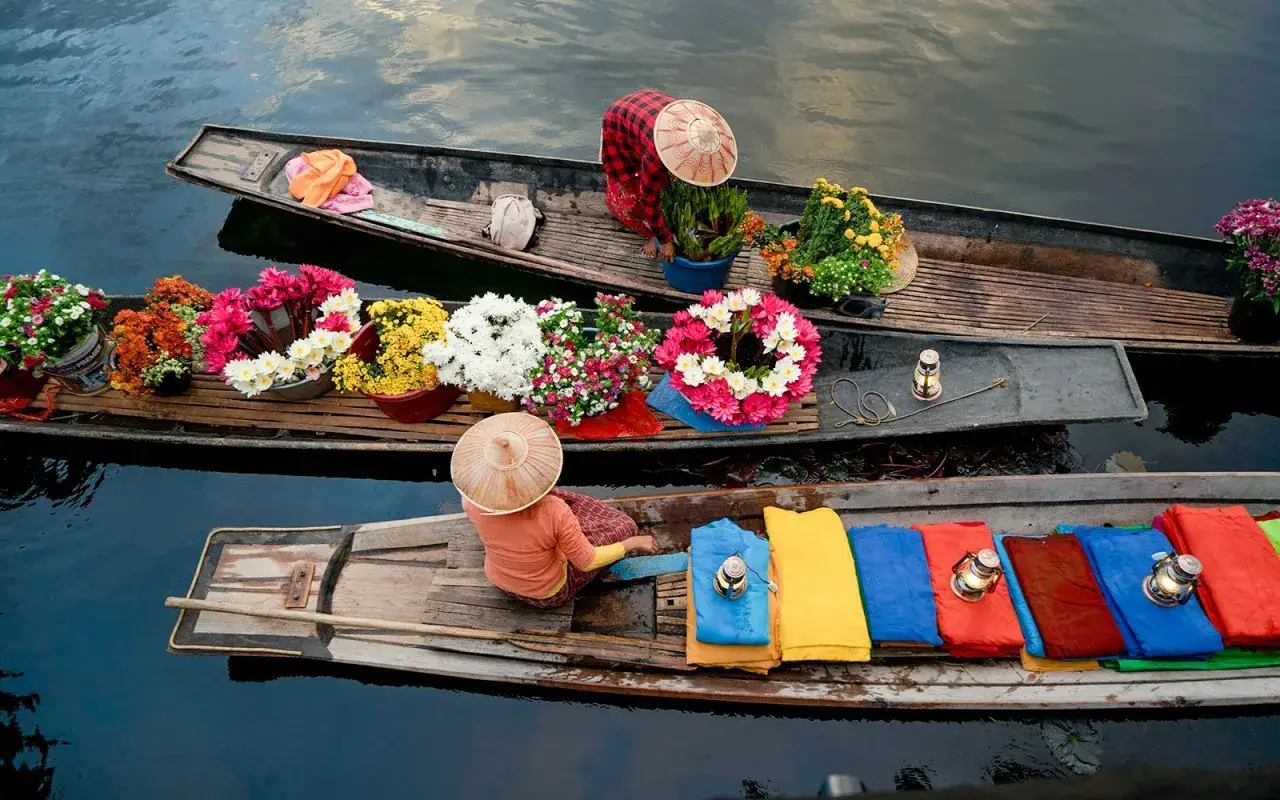 Bunte Blumen und Stoffe auf Booten auf einem schwimmenden Markt in Thailand.