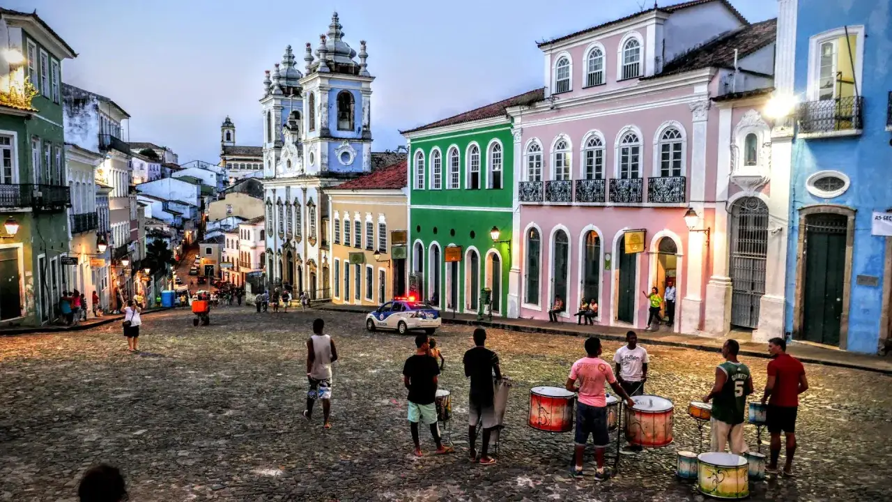 Bunte Kolonialhäuser in Salvador de Bahia, wo Musiker Trommeln spielen, während ein Polizeiauto vorbeifährt.