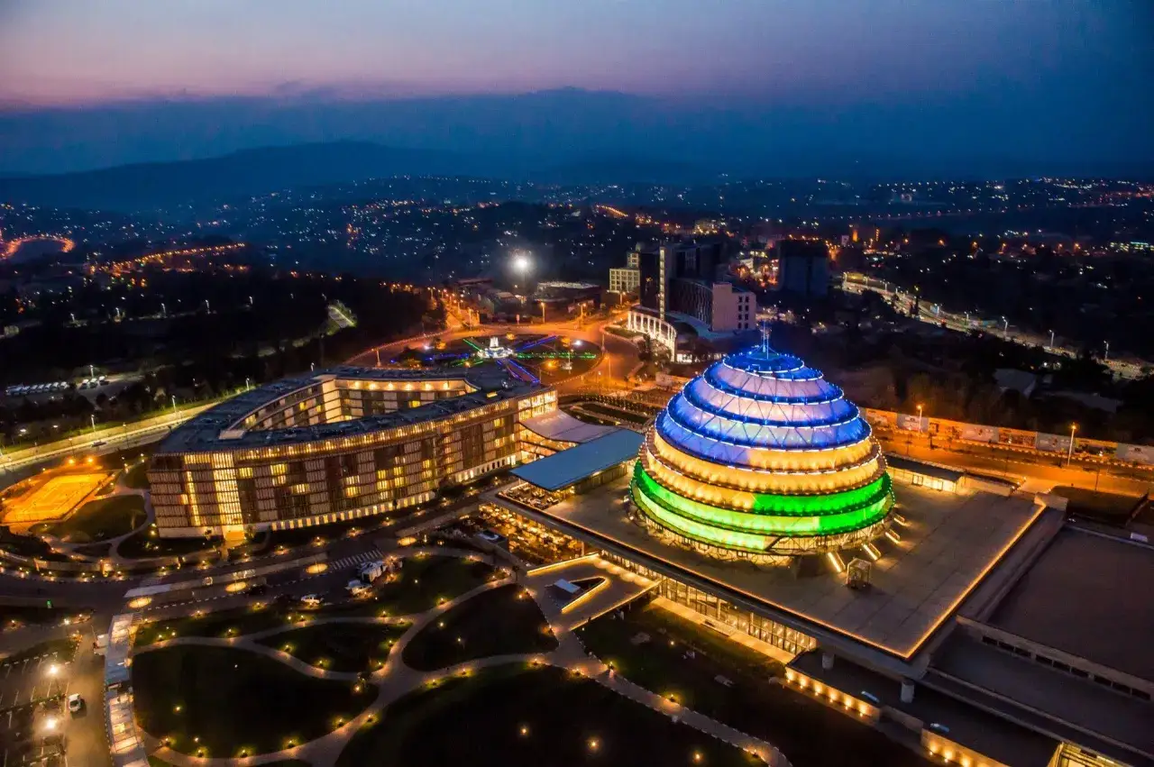 Nachtansicht von Ruanda, Kigali: Ein beleuchtetes, kuppelförmiges Gebäude in den Farben der ruandischen Flagge, umgeben von modernen Gebäuden und einer Stadtkulisse.