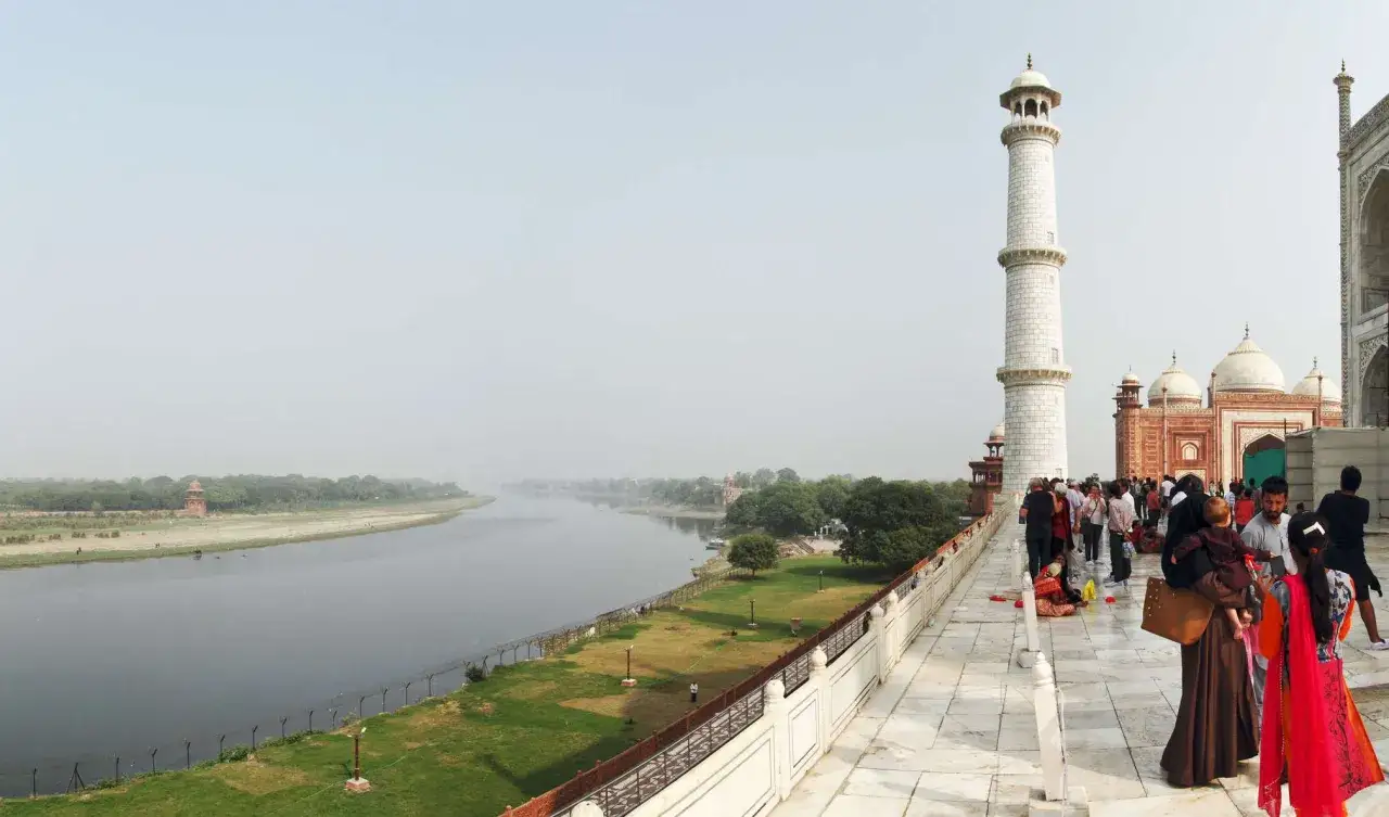 Besucher auf dem Gelände des Taj Mahal blicken auf den Fluss Yamuna. Ein Minarett und Kuppeln sind sichtbar.