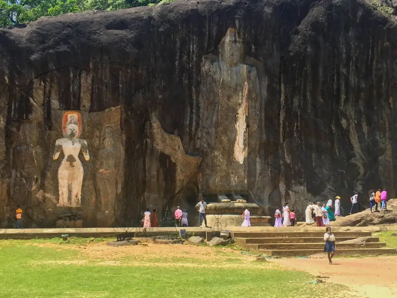 Felsreliefs in Jaffna, Sri Lanka: Eine Frauengestalt und eine stehende Buddha-Figur in einer Felswand, umgeben von Besuchern.
