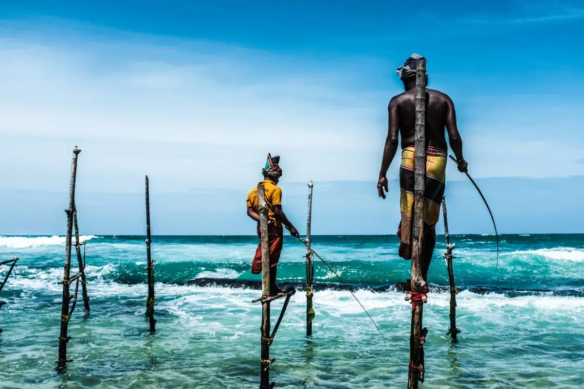 Zwei Stelzenfischer in Sri Lanka balancieren auf Pf&auml;hlen im Meer, um Fische zu fangen.