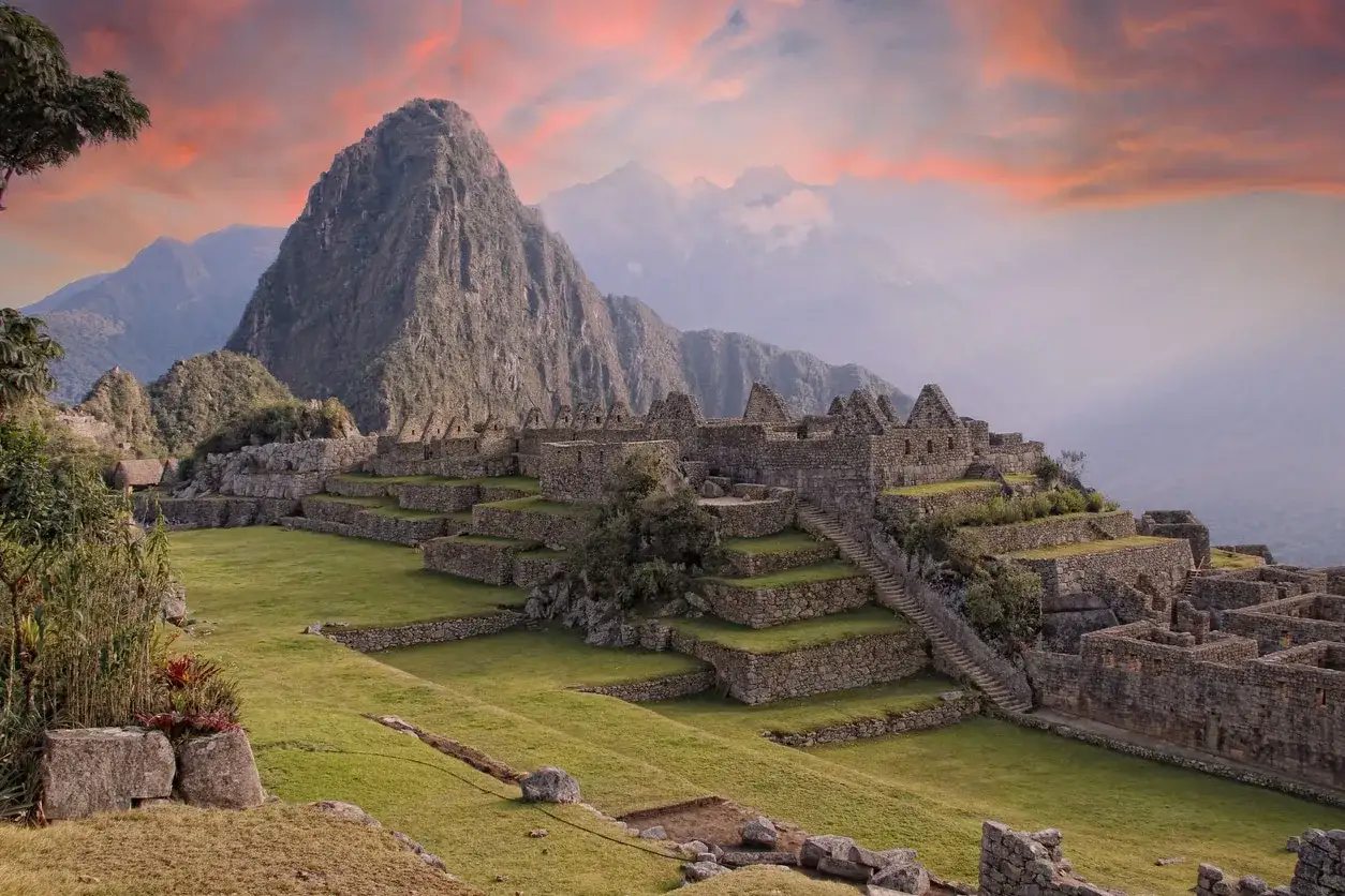 Sonnenuntergang über den Ruinen von Machu Picchu, die sich terrassenförmig an einen Berg schmiegen.