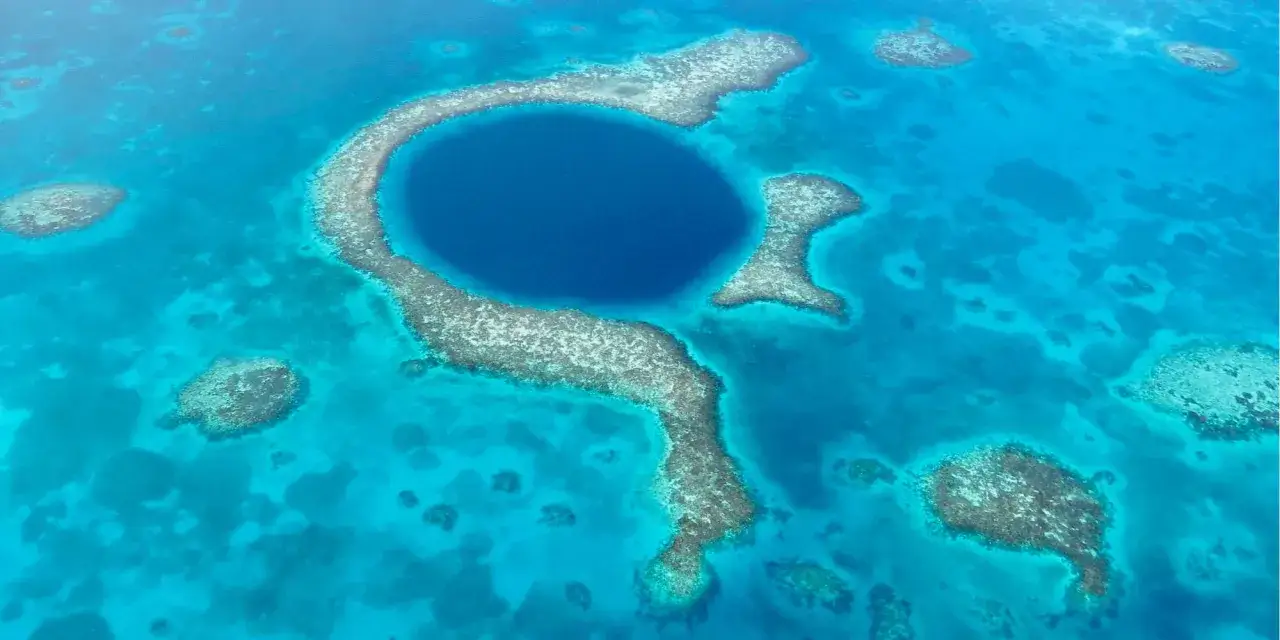 Das Belize Blue Hole, ein tiefblaues, kreisförmiges Loch im türkisfarbenen Meer, umgeben von Korallenriffen.
