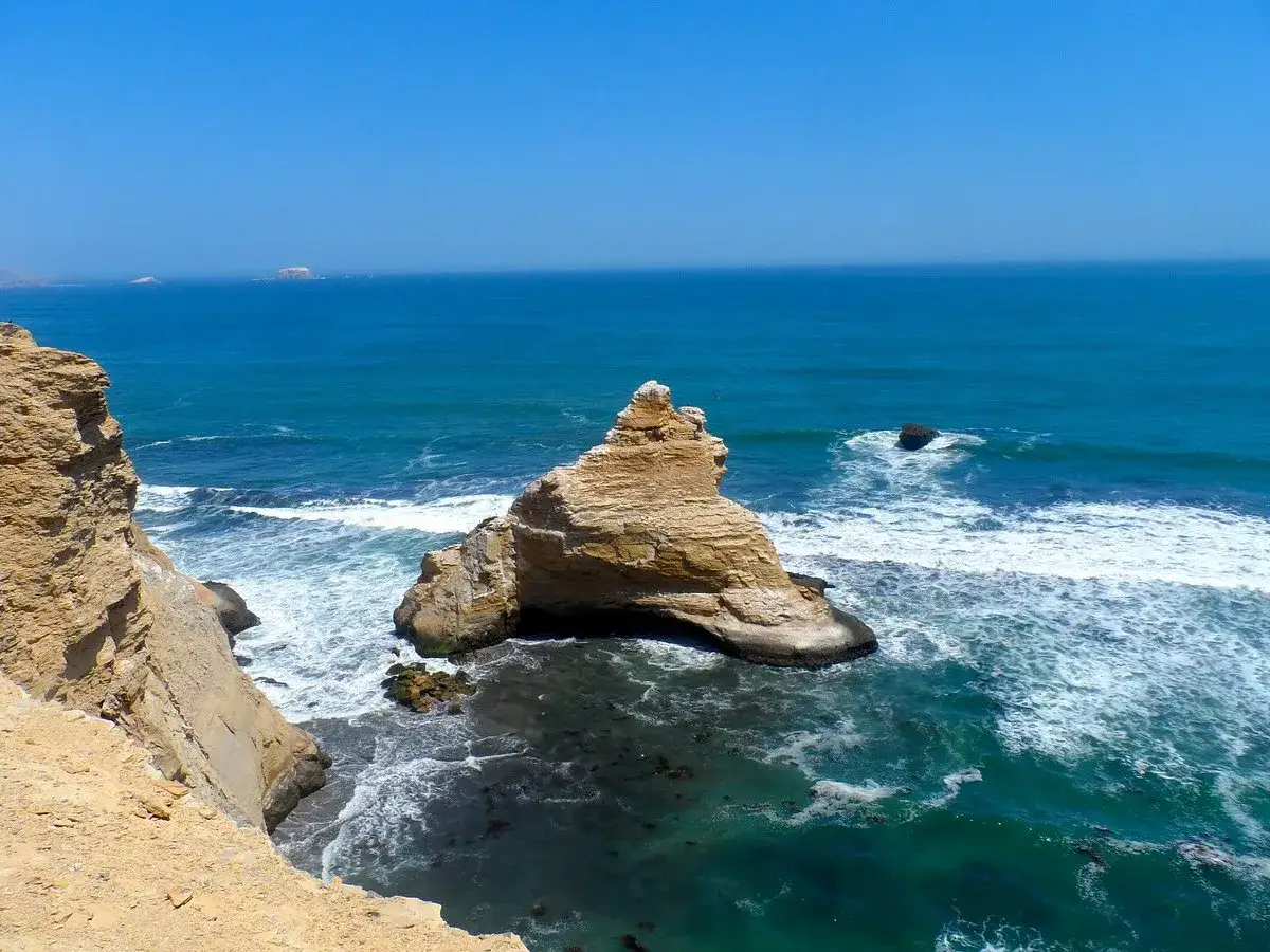 Felsformationen ragen aus dem türkisfarbenen Meer bei Paracas, Peru, empor. Wellen schlagen gegen die Küste.