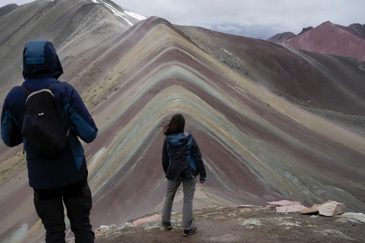 Zwei Wanderer bestaunen die farbenprächtigen Schichten des Regenbogenbergs in Peru.