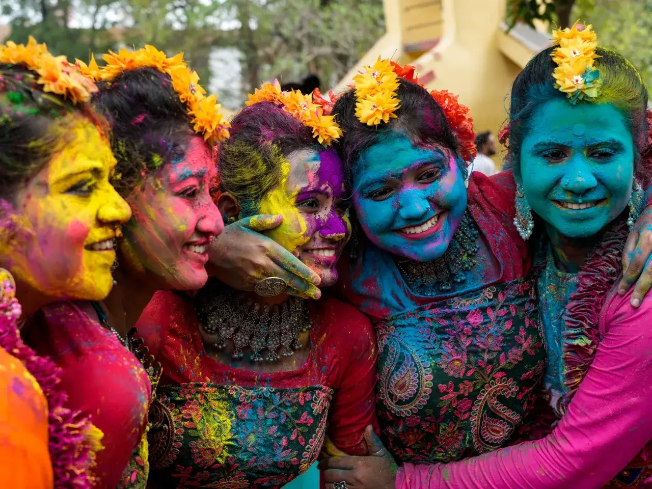 Freudige Gesichter, bedeckt mit bunten Pulvern, feiern den farbenfest indien. Blumen schmücken ihre Haare.