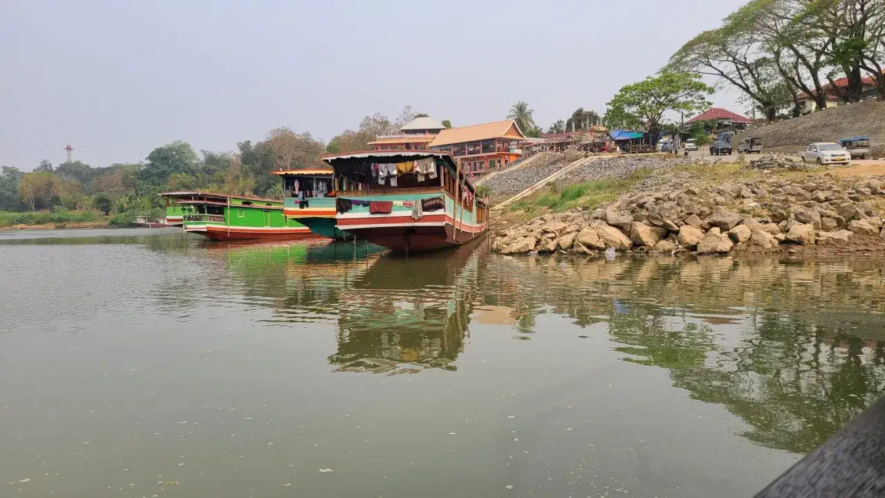Boote liegen am Ufer eines Flusses in Laos. Wäsche trocknet an einem der Schiffe.