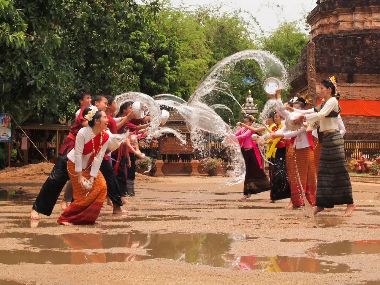 Fröhliches Thailand Neujahr mit Wasserschlachten und traditionellen Kleidern. Kinder und junge Erwachsene spritzen sich mit Eimern voller Wasser nass.