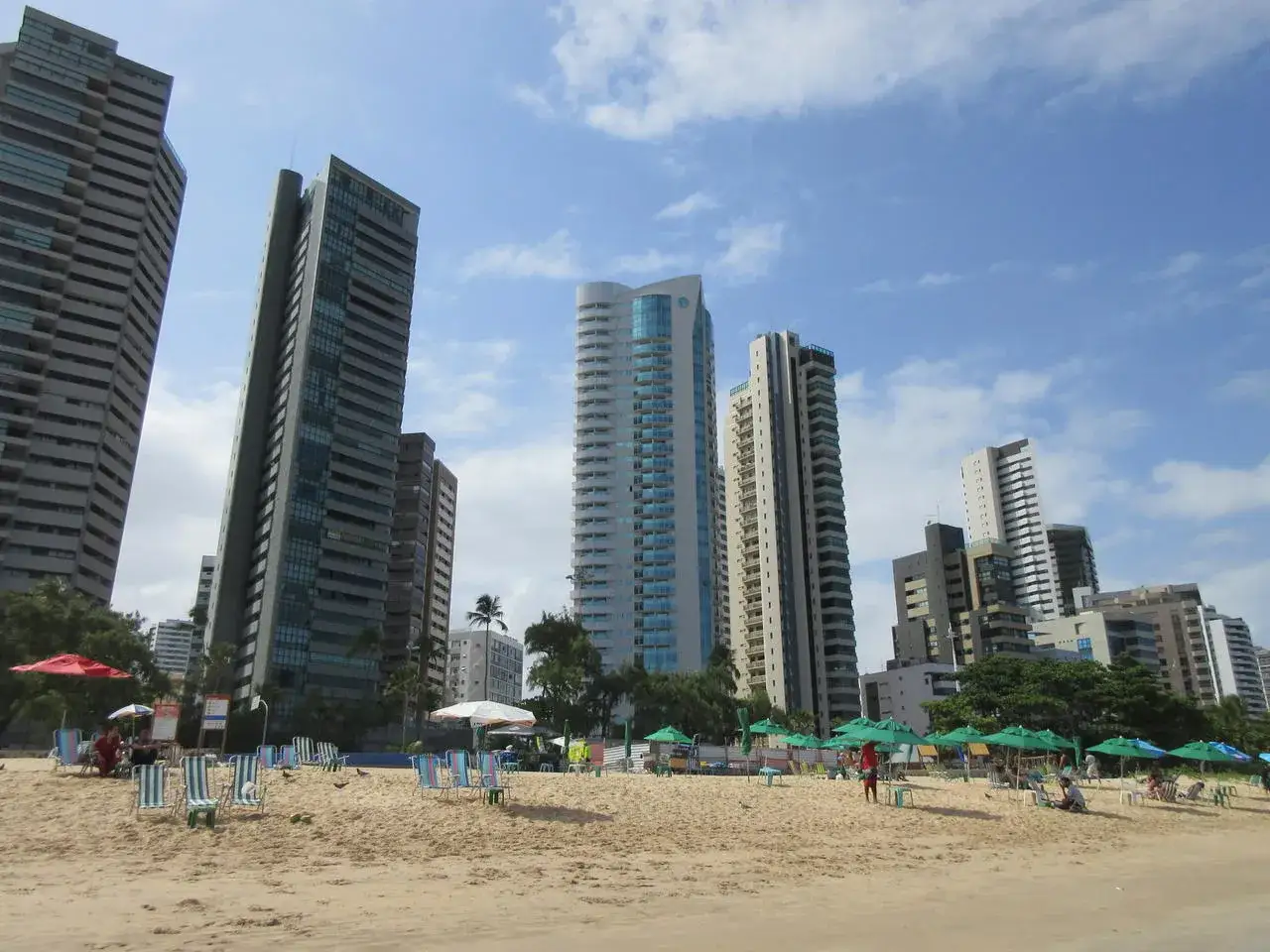 Hohe Gebäude ragen über den Sandstrand von Recife, Brasilien, auf, wo Liegestühle und Sonnenschirme auf Besucher warten.