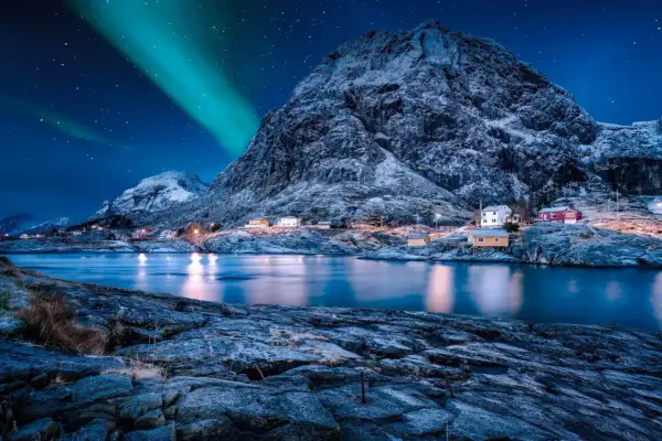 Nordkap Polarlichter tanzen über verschneite Berge und kleine Häuser am Fjord. Ein magischer Anblick!