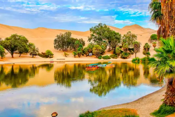 Oase Huacachina bei Ica, Peru, mit Sanddünen, Palmen und einem See voller bunter Boote.